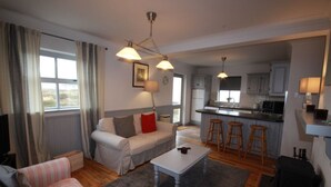 Una sala moderna con un sofá, una mesa de centro y una zona de cocina con taburetes de bar.