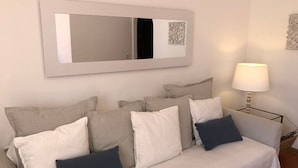 Un sofá de tonos neutros con varios cojines, un espejo montado en la pared y una lámpara de pie.