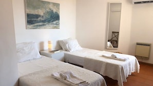 Habitación de hotel con dos camas, un cuadro en la pared, una mesita de noche con lámpara, un espejo y un radiador.