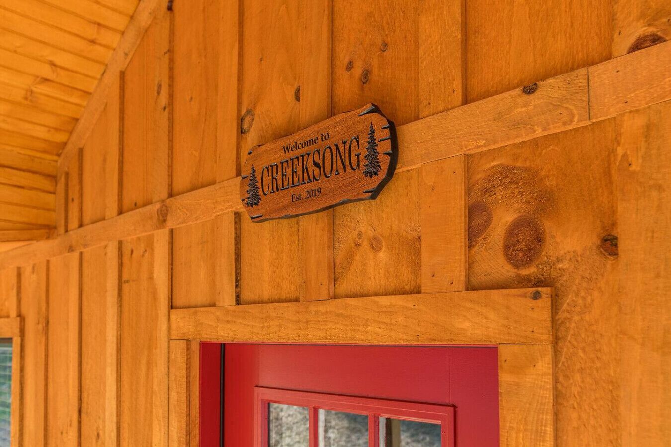 Un mur extérieur en bois, avec une porte rouge et une enseigne sur laquelle on peut lire : « Bienvenue chez CREEKSONG, fondé en 2019 ».