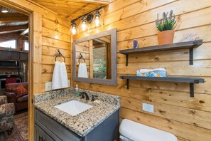A wooden cabin bathroom with a granite sink, a mirror, and two shelves with toiletries.