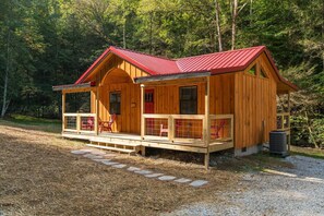A wooden cabin with a red roof, a porch with red chairs, and a small window.