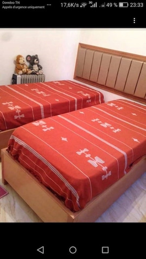 Two beds with red bedspreads feature a white pattern, positioned against a wall with a headboard.