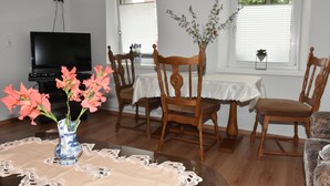 A dining area with a table, chairs, a vase with flowers, and a television in the background. - King cottage in the center (Königsbrück)