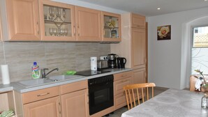 A kitchen with wooden cabinets, a dishwasher, a coffee maker, and a dining table with chairs. - King cottage in the center (Königsbrück)