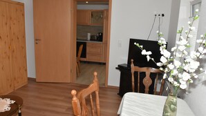A room with a wooden wardrobe, a dining table with a vase of flowers, and a kitchen visible through an open door. - King cottage in the center (Königsbrück)