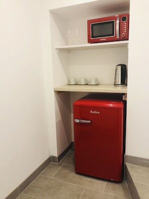 Compact kitchenette with a refrigerator, microwave, and kettle.