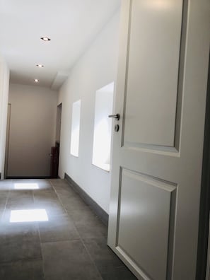 Corridors feature doors with keyholes and handles, large tile flooring, and windows on either side.