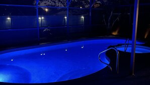 Ein Schwimmbecken mit gewölbter Kante, umgeben von einer Glaskonstruktion mit Metallrahmen.