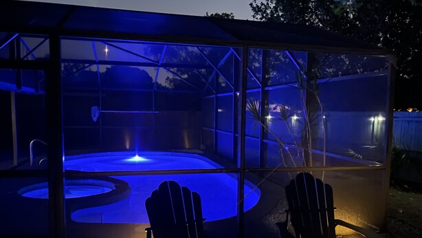 Ein von Glas umschlossener Whirlpoolbereich mit zwei Adirondack-Stühlen, einer eingebauten Bank und einem kleinen Wasserfall.