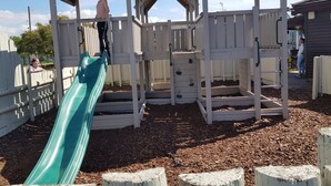 Une structure de jeu en bois comprenant un toboggan, des éléments d’escalade et un espace abrité.