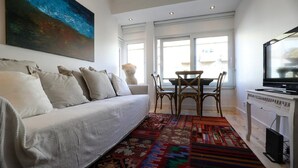 Una sala moderna con un sofá, un tapete estampado, una mesa de comedor con sillas y un televisor.