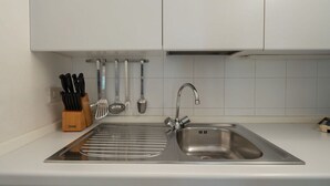A kitchen with a stainless steel sink, a knife block, and various utensils on the wall. - Garden Apartment (Venice)