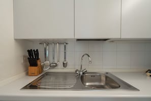 Een keuken met een roestvrijstalen spoelbak, een messenblok en verschillende keukengerei aan de muur.