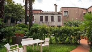 A patio with a table and chairs, surrounded by greenery and a brick pathway. - Garden Apartment (Venice)