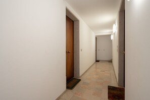 A hallway with white walls, a wooden door, and a tiled floor.