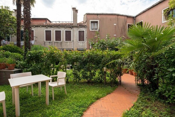 A courtyard with a brick pathway, white chairs, and potted plants.