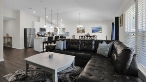 Ein modernes Wohnzimmer mit einem schwarzen Ledersofa, einem weißen Couchtisch und einem Essbereich mit einer Küche im Hintergrund.