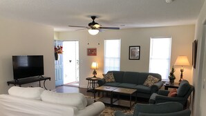 A living room with a flat-screen TV, a ceiling fan, a sofa, a coffee table, and a lamp.