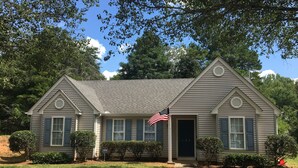 A two-story house with a gabled roof, a front porch, and an American flag.