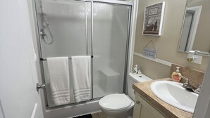 Un baño con cabina de ducha de vidrio, inodoro, lavabo con encimera y espejo.