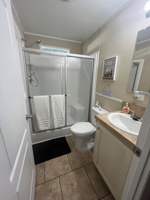 Un bagno con box doccia in vetro, un water, un lavabo con piano di appoggio e uno specchio.