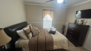 Un dormitorio con cama, cómoda, ventilador de techo y ventana con cortinas.