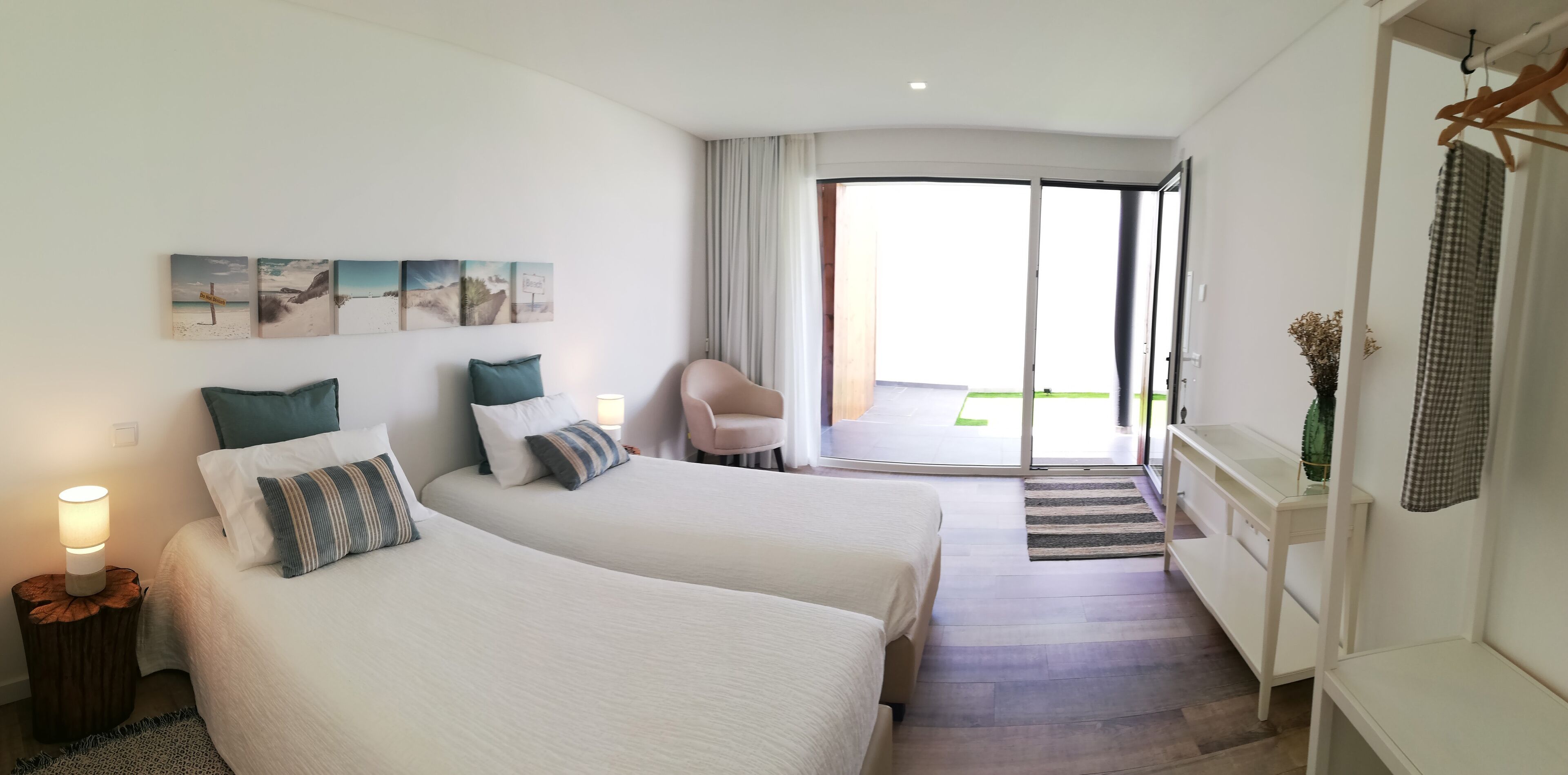 Habitación de hotel con dos camas, una silla, un escritorio y vistas a un área exterior a través de una puerta corrediza de vidrio.