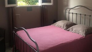 Un lit simple avec un cadre en métal et une couvre-lit rose, dans une pièce dotée d’une fenêtre.
