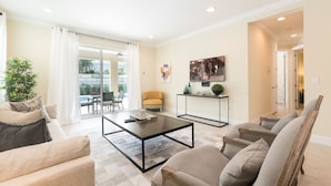 A spacious living room with a sofa, armchairs, a coffee table, and a dining area with chairs. There is a sliding glass door leading to an outdoor area. - Fabulous Disney Vacation Home - 5 Minutes From Disney (Kissimmee)