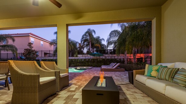 A patio area with wicker furniture, a fire feature, and a view of a pool and palm trees. - Fabulous Disney Vacation Home - 5 Minutes From Disney (Kissimmee)