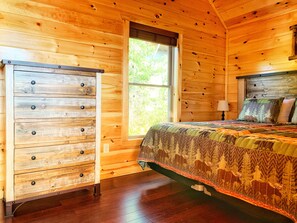 Un dormitorio de cabaña de madera con cama, cómoda y ventana.