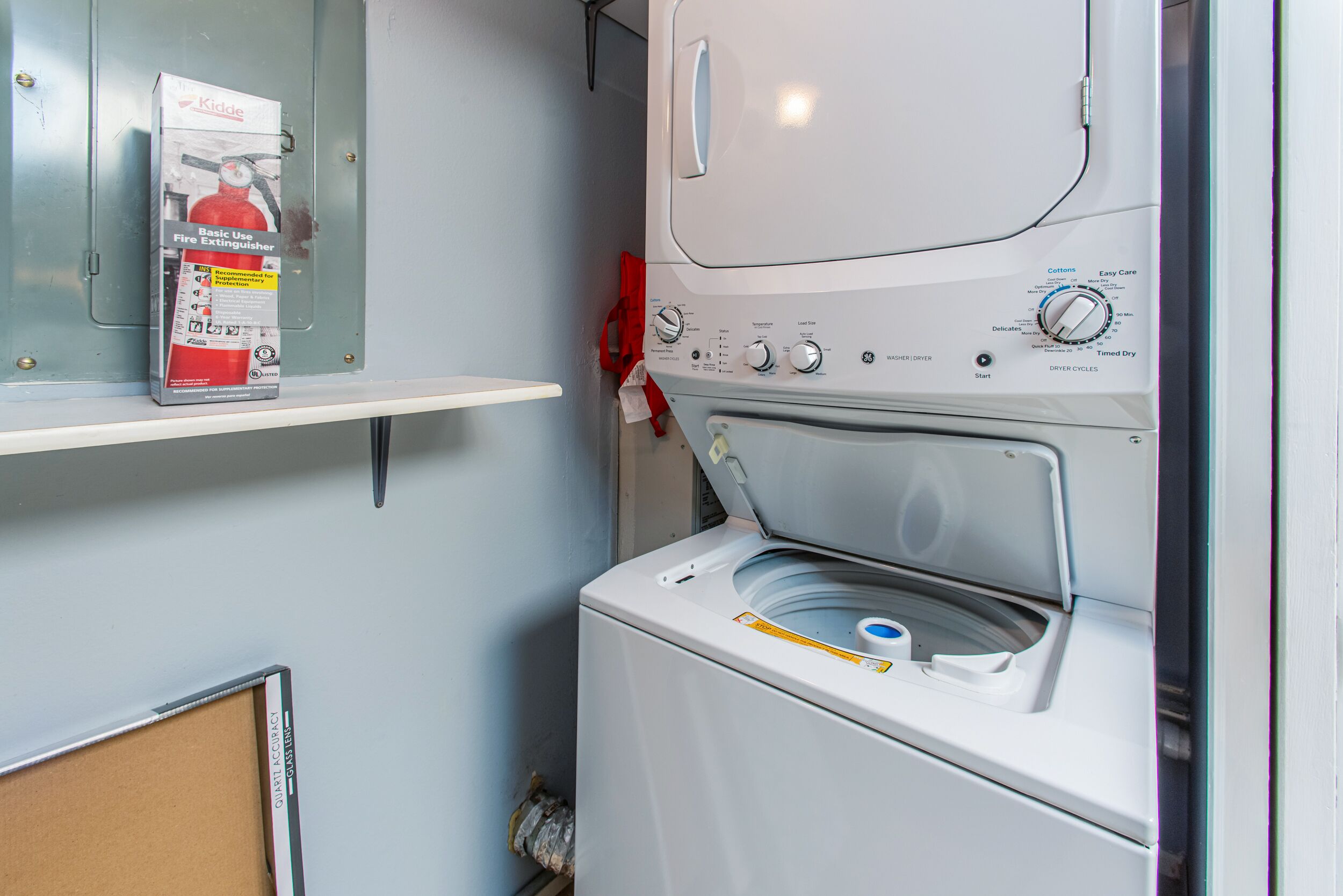 A compact laundry area with a washing machine and a shelf holding a fire extinguisher.