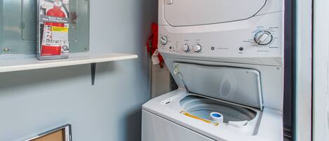 A compact laundry area with a washing machine and a shelf holding a fire extinguisher.