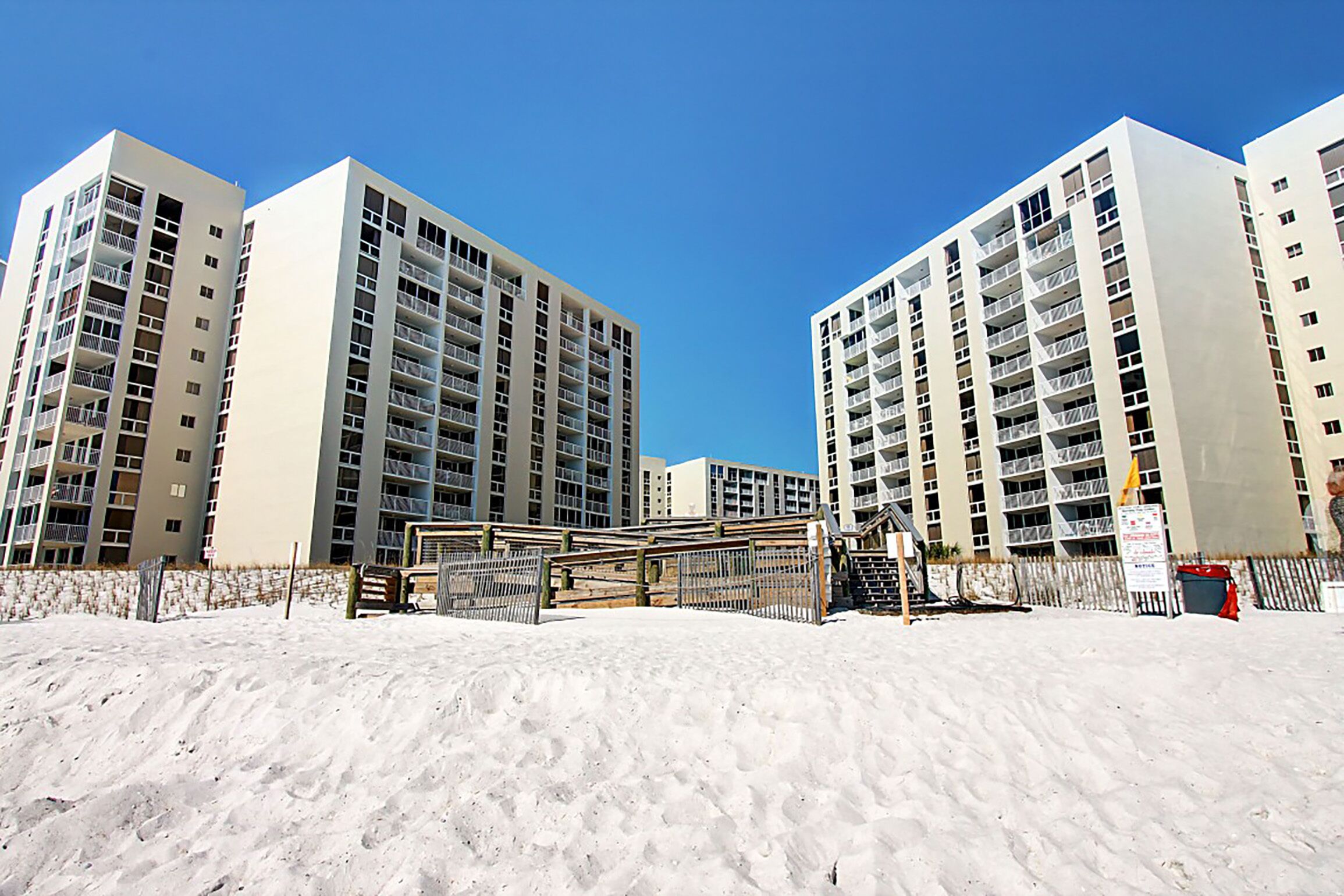 A beachfront hotel with multiple high-rise buildings, a sandy beach, and a clear blue sky.