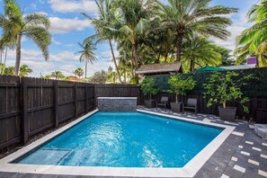 A rectangular swimming pool with a stone accent wall, surrounded by a wooden fence and palm trees. - Mid-Centrury Oasis | 1 Block to Ft Lauderdale Beach (Fort Lauderdale)