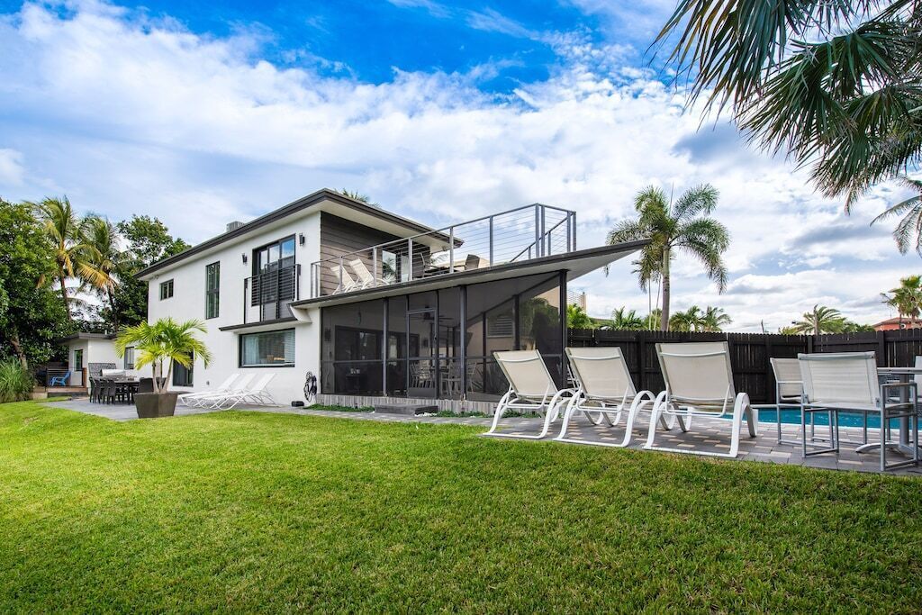 Una casa moderna con piscina, sillones blancos y un césped cuidado.