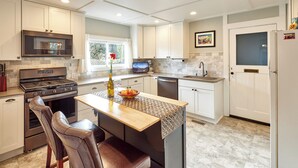 A modern kitchen with white cabinetry, a built-in oven, a microwave, and a dishwasher. There is a wooden island with a bottle of olive oil and a bowl of fruit. - Historic Silverton Home 5 BR, 6 Bath.  Ask about 6th & 7th bedroom add-ons. (Silverton)