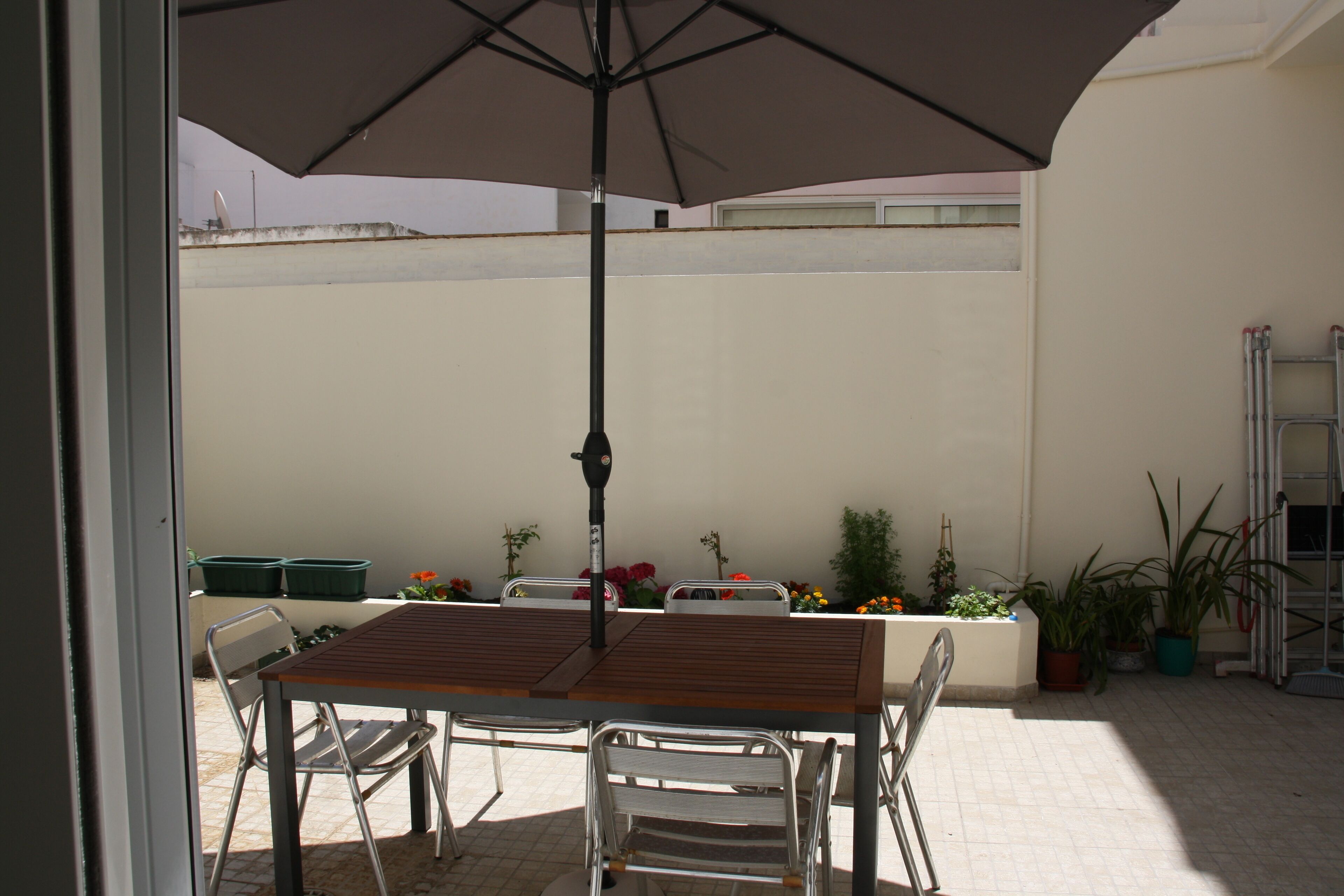 Une terrasse extérieure avec une table et des chaises en bois, un grand parasol et des plantes en pot.