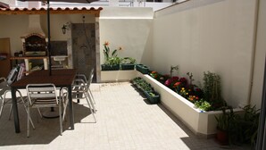 A patio area with a wooden table and chairs, a tiled floor, a small sink, and a variety of potted plants.