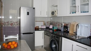 A kitchen with a stainless steel refrigerator, a washing machine, a microwave, and a sink.