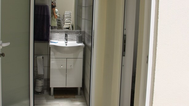 A narrow hallway with a bathroom featuring a sink, mirror, and towel rack.