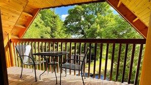 Um deck de madeira com mesa e cadeiras, cercado por um corrimão de madeira, com vista para uma paisagem verde.