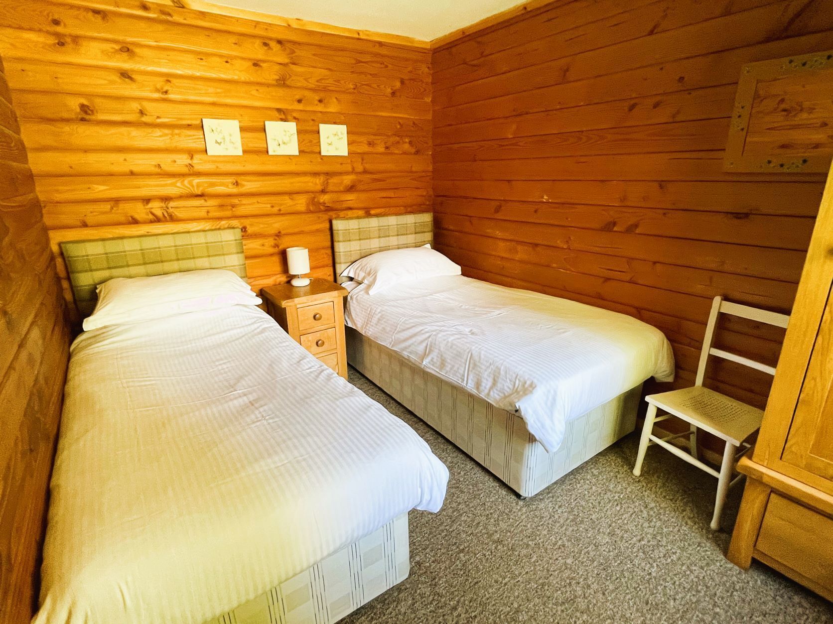 A room with two beds, a nightstand, a chair, and wooden walls.