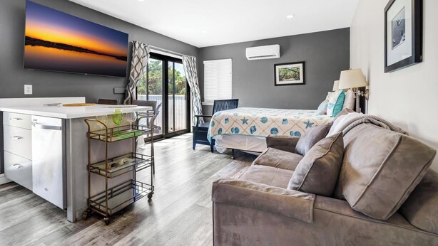 Una habitación moderna con kitchenette, una cama con colcha estampada y un amplio ventanal con cortinas.