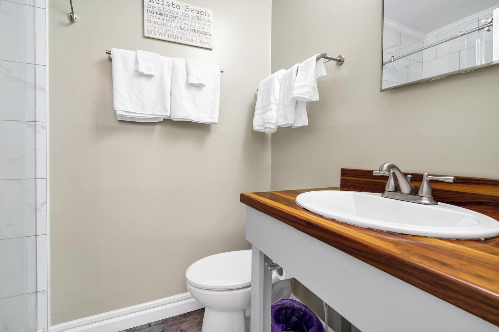 Ein Badezimmer mit einer weißen Toilette, einem hölzernen Waschtisch mit Waschbecken und zwei weißen Handtüchern, die an Handtuchhaltern hängen.
