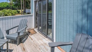 Una terraza de madera con dos sillas Adirondack y un ventanal corredera que da a un porche cubierto.