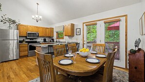 A modern kitchen with wooden cabinets, a stainless steel refrigerator, and a dining area with a wooden table and chairs.