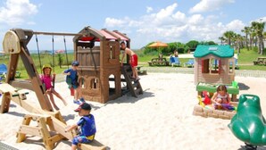 Ein Kinderspielbereich mit Schaukeln, Klettergerüsten und einem kleinen Spielhaus.