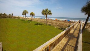 Ein Strand mit einer Holzpromenade, Palmen und Strandsonnenschirmen.